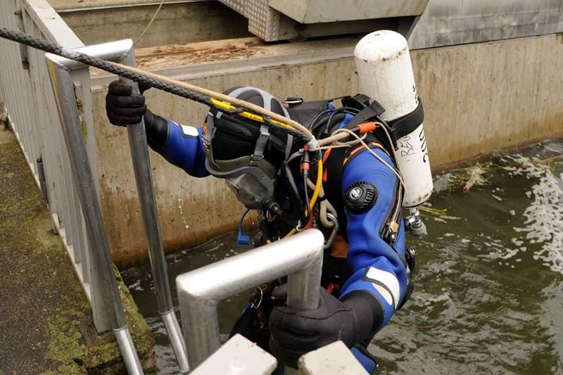 Taucher der LEW Wasserkraft steigt mit Tauchausrüstung ins Wasser.